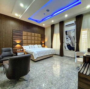 A modern hotel room with a large bed, a desk, a chair, and a sofa. - H5 Hotel and Apartments (Enugu)