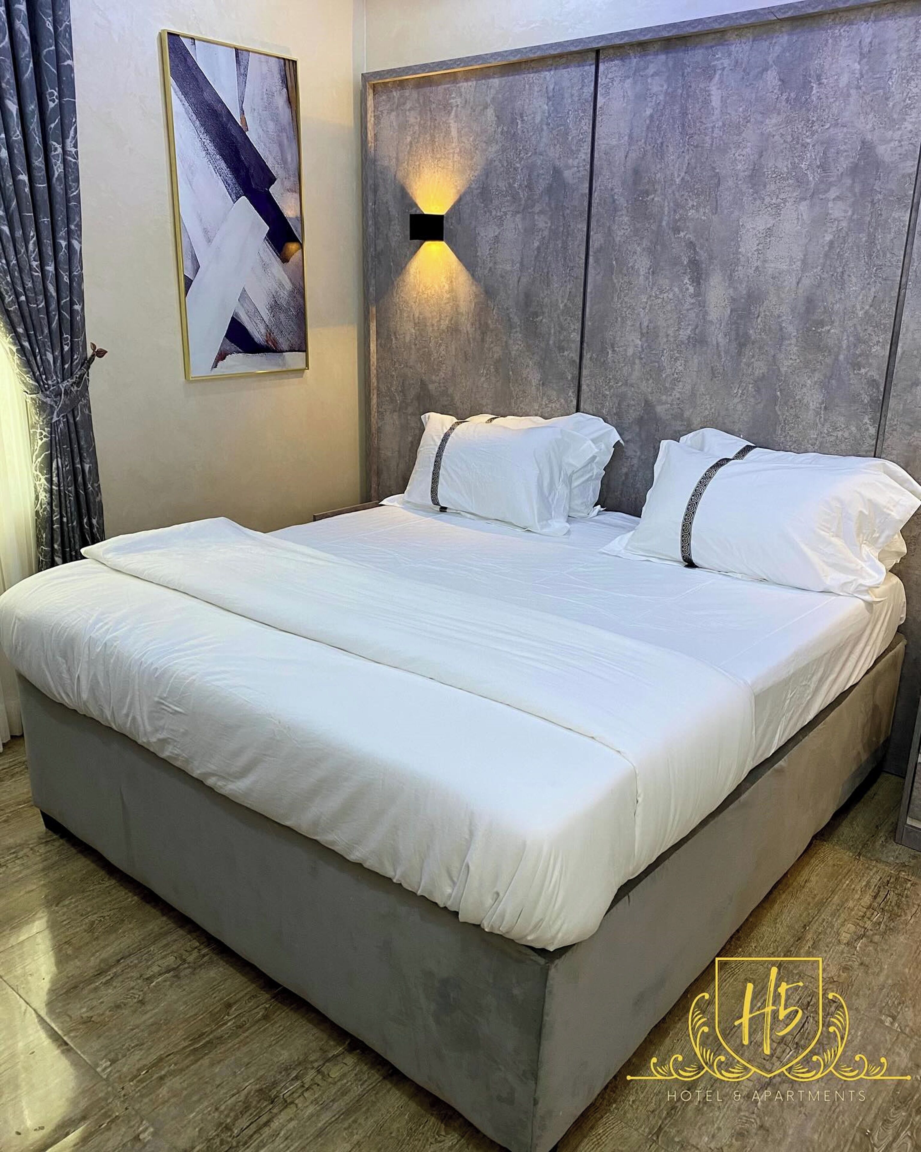A modern bedroom with a large bed, grey walls, and a framed abstract painting.