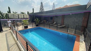 A swimming pool with a tiled deck, surrounded by lounge chairs and a covered seating area.
