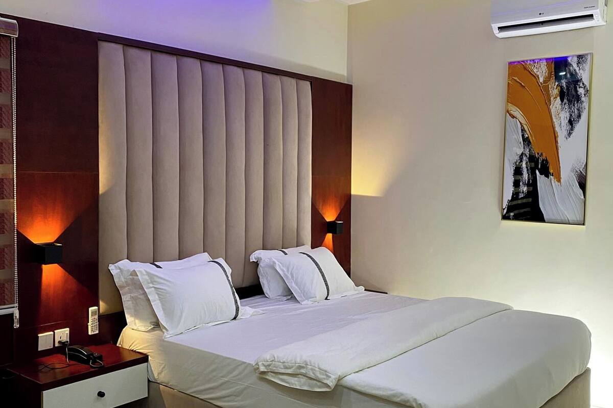 A modern hotel room with a large bed, a bedside table with a phone, and a wall-mounted air conditioner.
