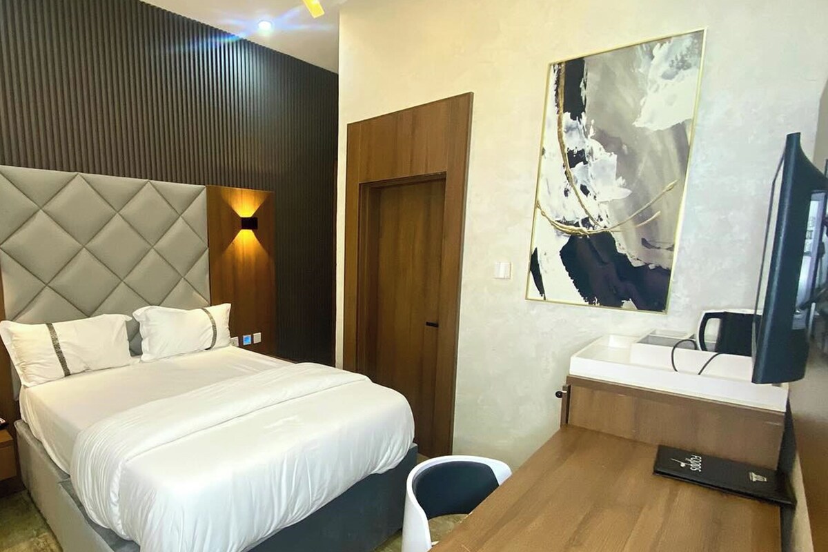 A modern hotel room with a large bed, bedside tables, a desk, and a television.