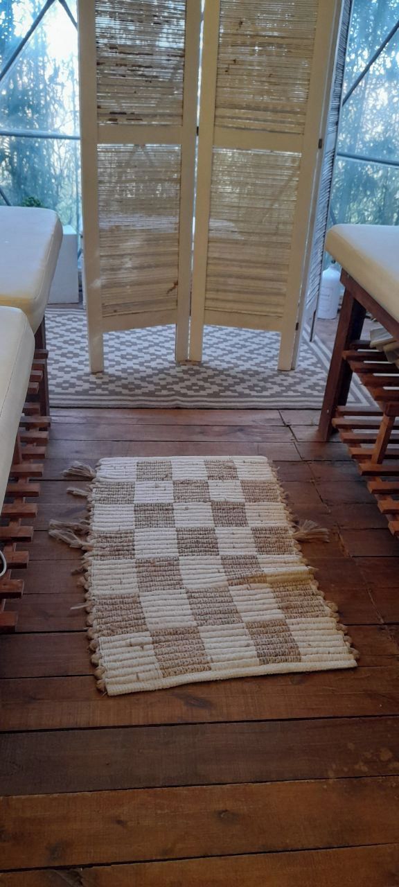 A wooden deck with a checkered rug, wooden chairs, and a woven partition.