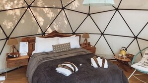 Um quarto aconchegante com parede estampada em padrão geométrico, uma cama de madeira, um lustre pendente e piso de madeira.
