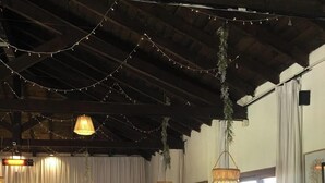 Amplo espaço interno com teto alto, luminárias de vime suspensas e área de estar com sofás e cadeiras.