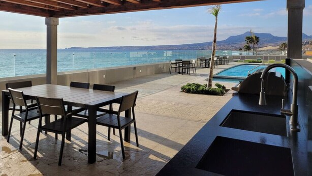 Un patio exterior con una pérgola de madera, una piscina y vistas al mar.