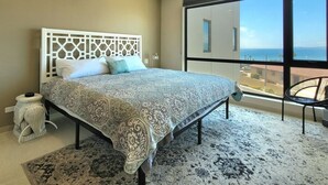 Un dormitorio con cama, ventilador de techo, ventana grande con vistas y una silla.
