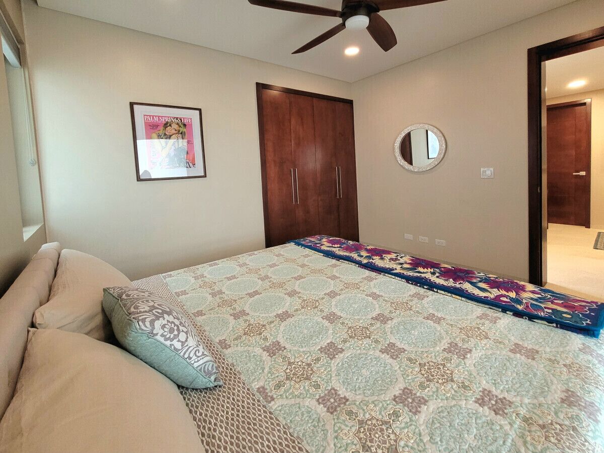 Quarto com cama, ventilador de teto, guarda-roupa, espelho e um quadro na parede.