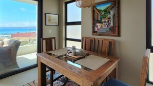 Un comedor con una mesa de madera, sillas y vista al océano a través de amplios ventanales.