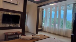 A hotel room with a flat-screen TV, air conditioning, a massage table with towels, a small table with items, and a large window with curtains. - Sami Resort  (Tirupattur)