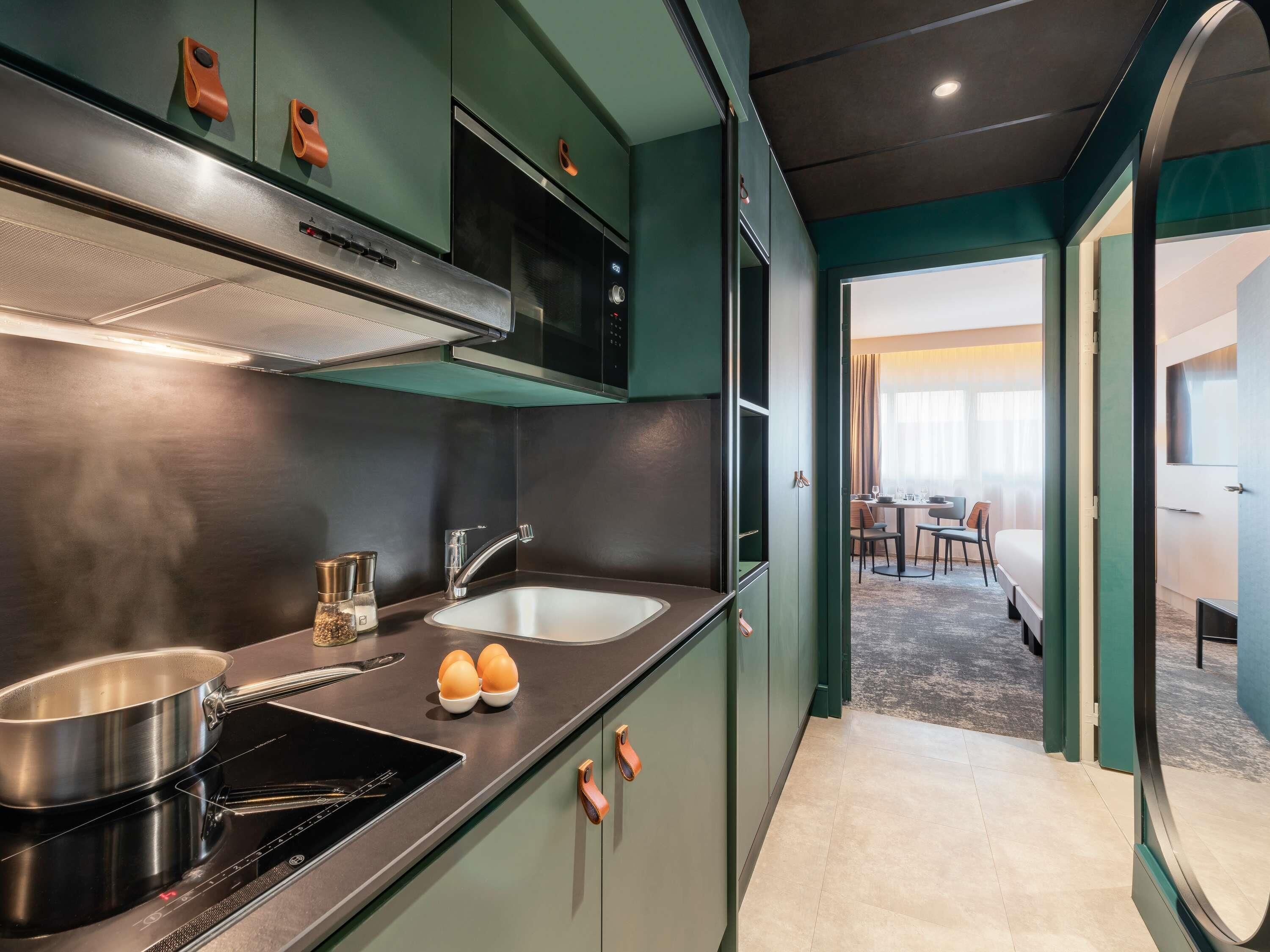 A compact kitchen with a microwave, stove, and sink. There is a dining area with a table and chairs visible through an open doorway.