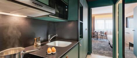 A compact kitchen with a microwave, stove, and sink. There is a dining area with a table and chairs visible through an open doorway.