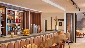 Un espace bar avec un comptoir en bois, de nombreuses bouteilles d’alcool, un verre de bière et des tabourets de bar.