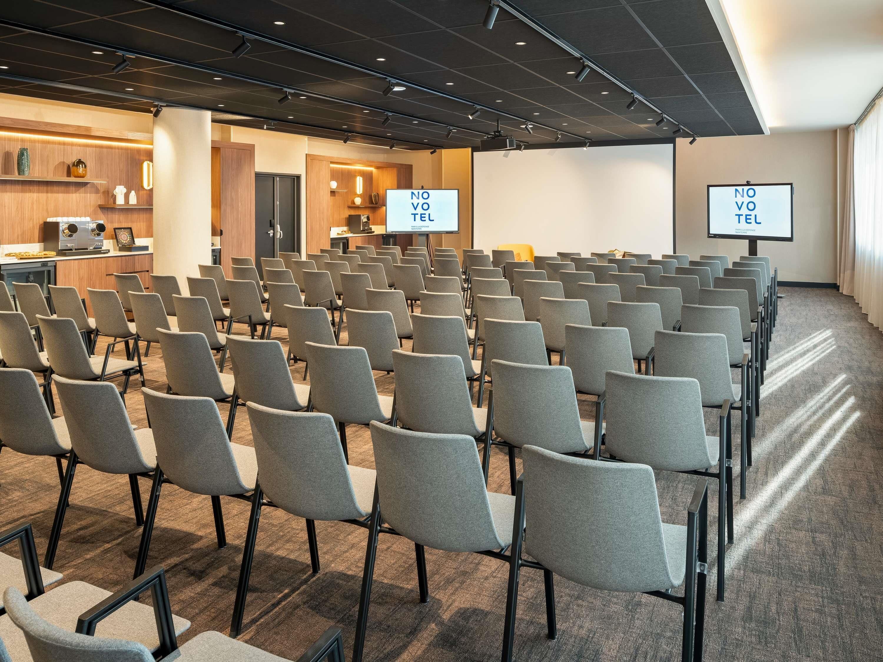 Un salón de conferencias con hileras de sillas, un atril y una pantalla de proyector.