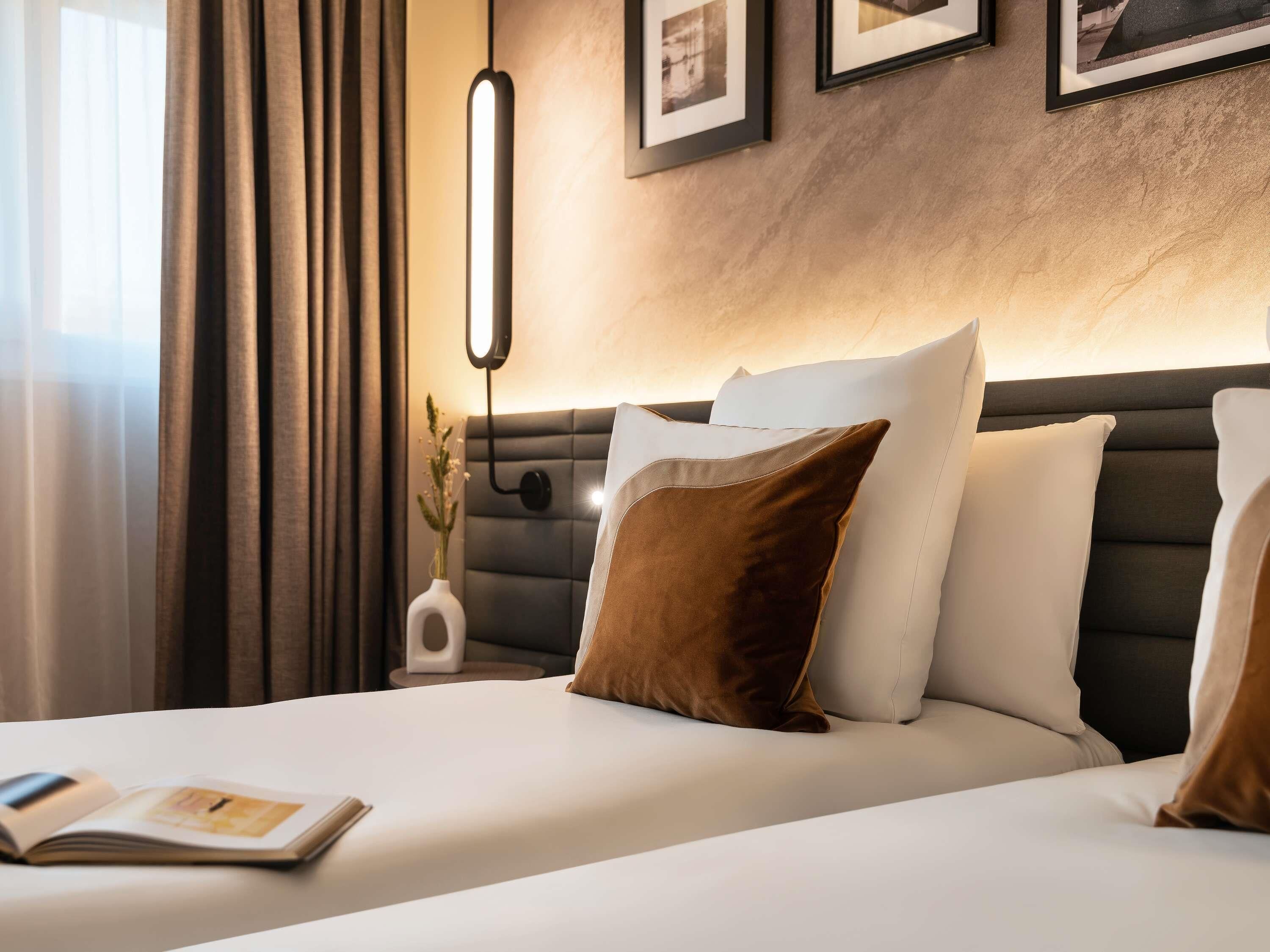 A hotel room with a bed, a bedside table, a lamp, and framed pictures on the wall.