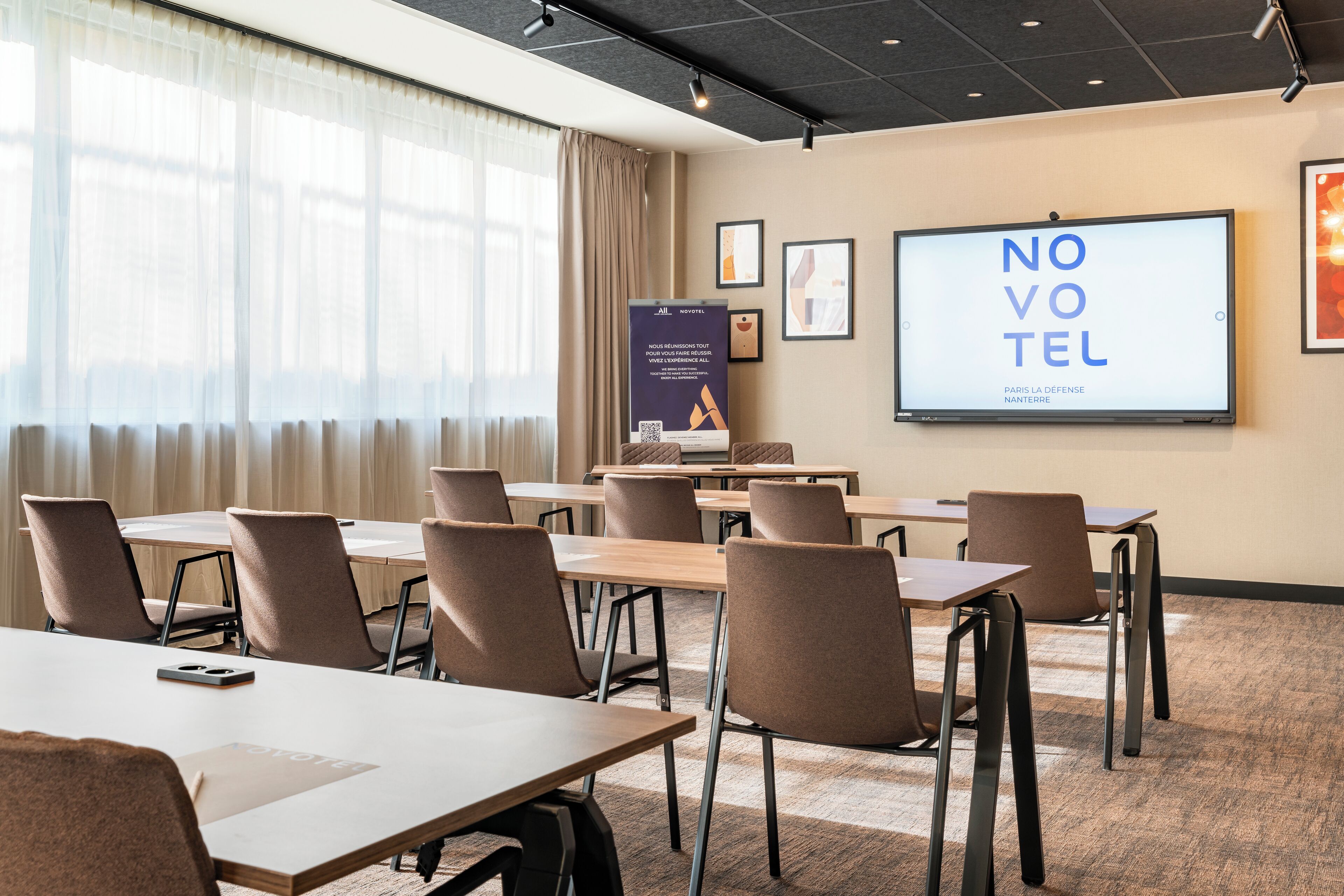 A conference room with a large screen displaying 'NOVOVOTEL' and 'PARIS LA DEFENSE NANTERRE'.