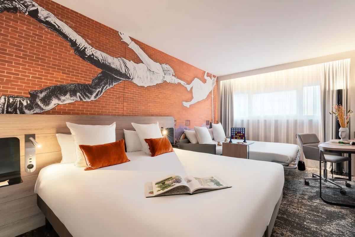 A hotel room with a large bed, a desk, a chair, and a window with curtains.