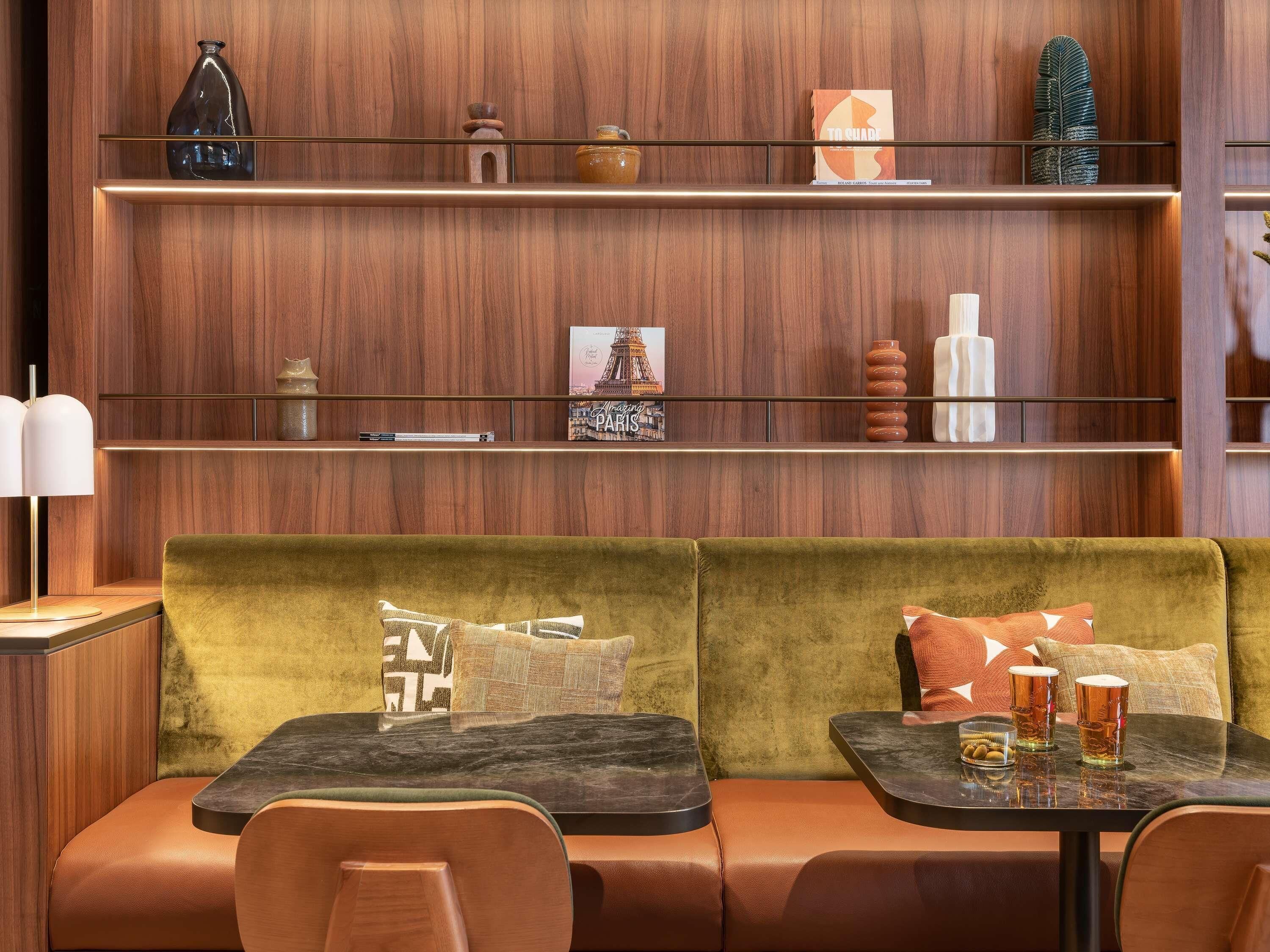 A modern interior with a wooden wall, a green cushioned bench, and a table with two glasses and a small bowl.