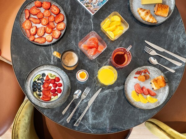 Una mesa de desayuno con frutas, pasteles y bebidas varias.