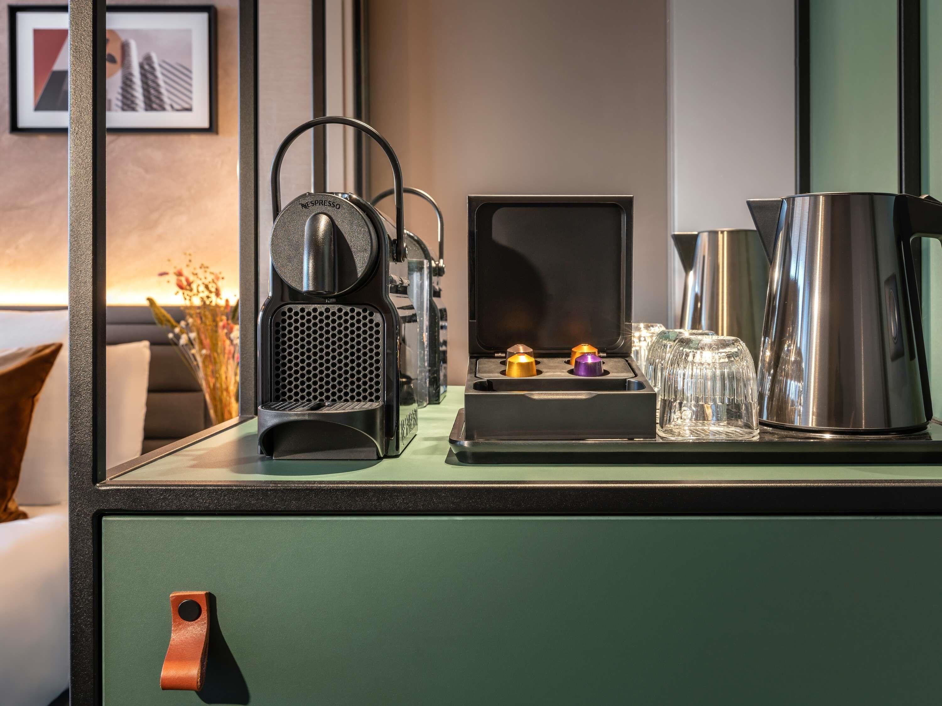 A coffee machine, a kettle, and a glass set on a counter with a green cabinet.
