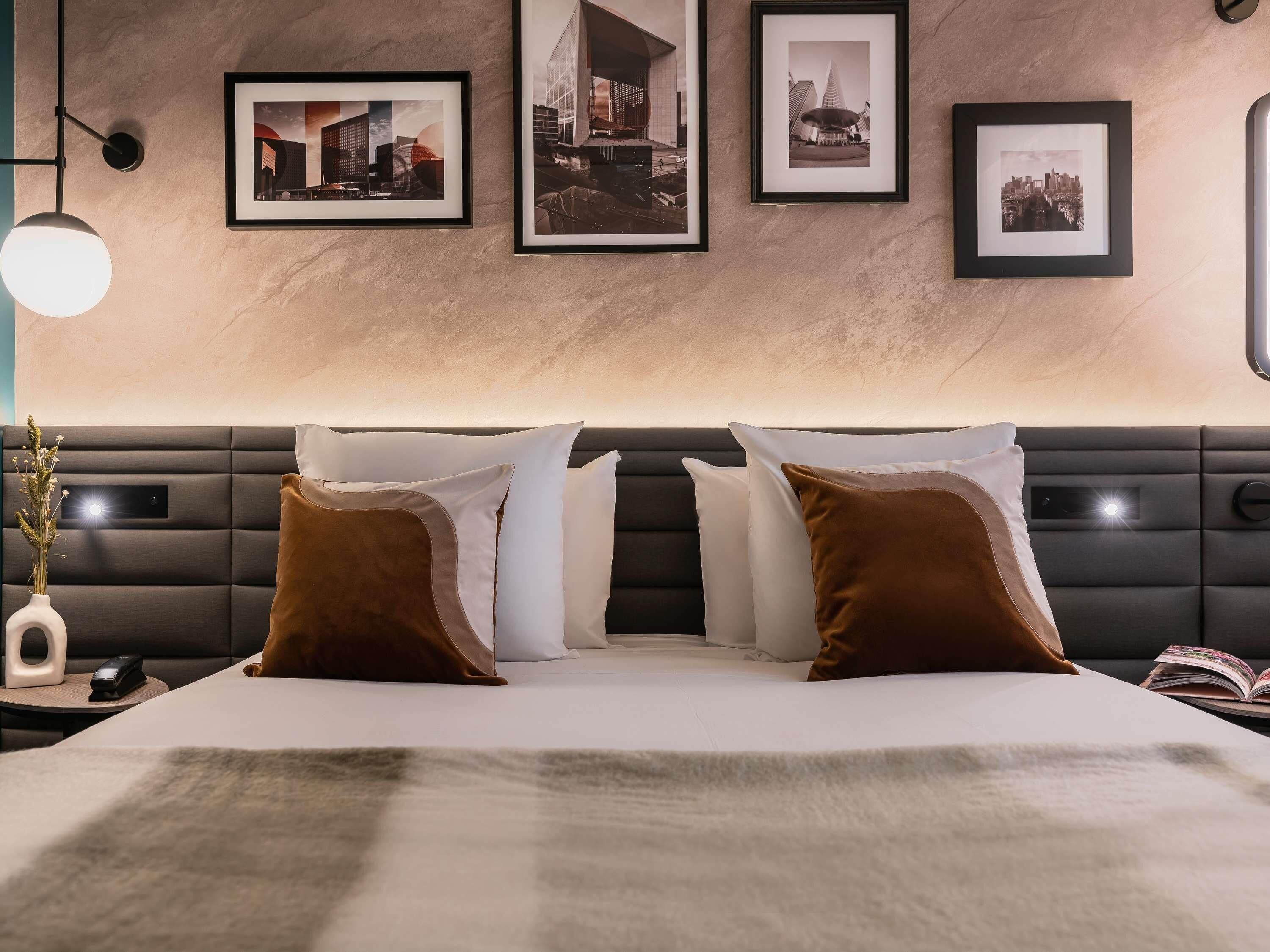 A modern hotel room with a large bed, a headboard, and framed pictures on the wall.