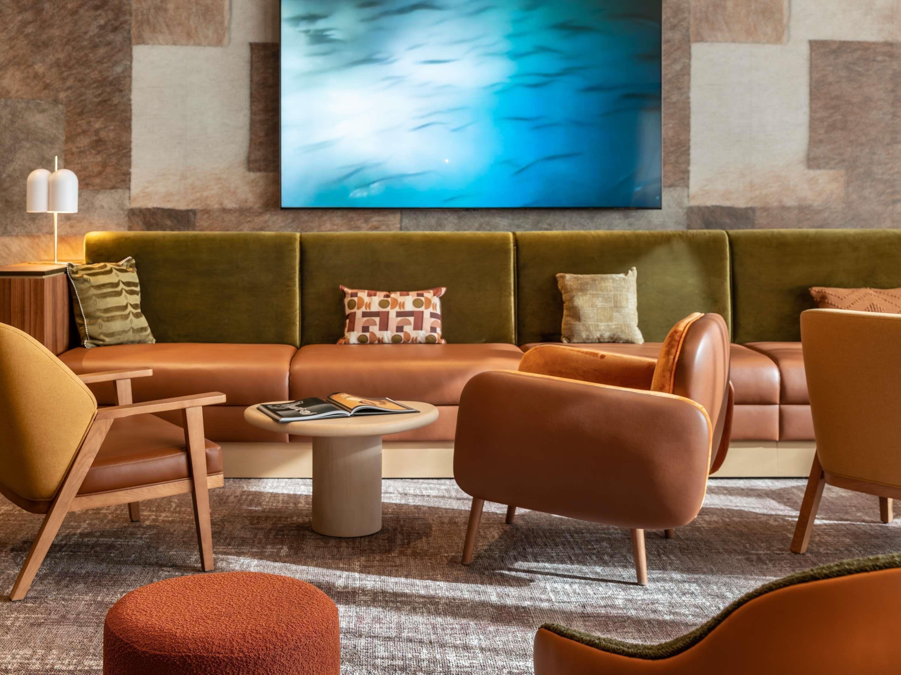 Una sala moderna con un sofá verde, una mesa de centro de madera y sillones naranjas.