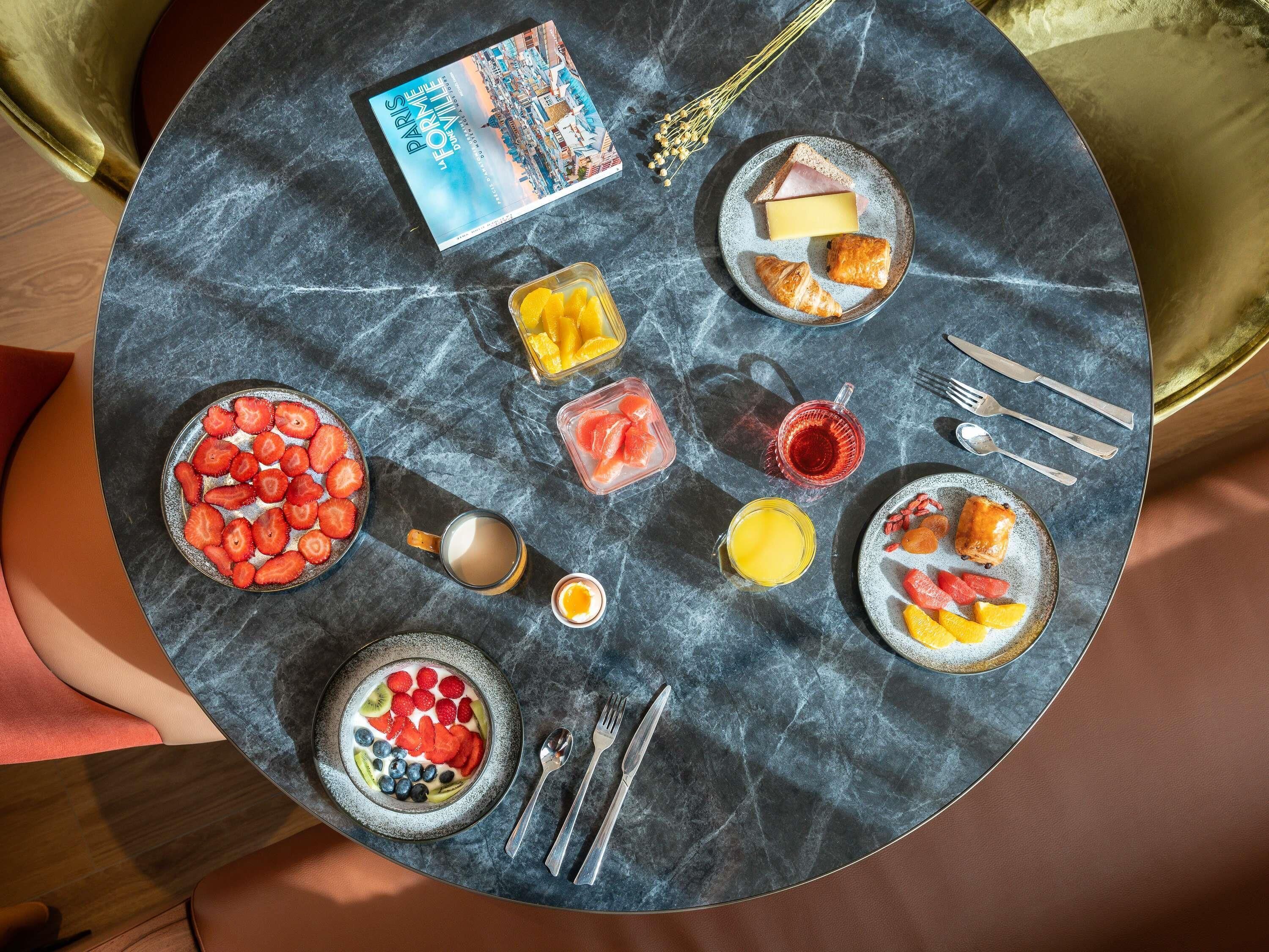 A round table with a book, plates of food, and cutlery.