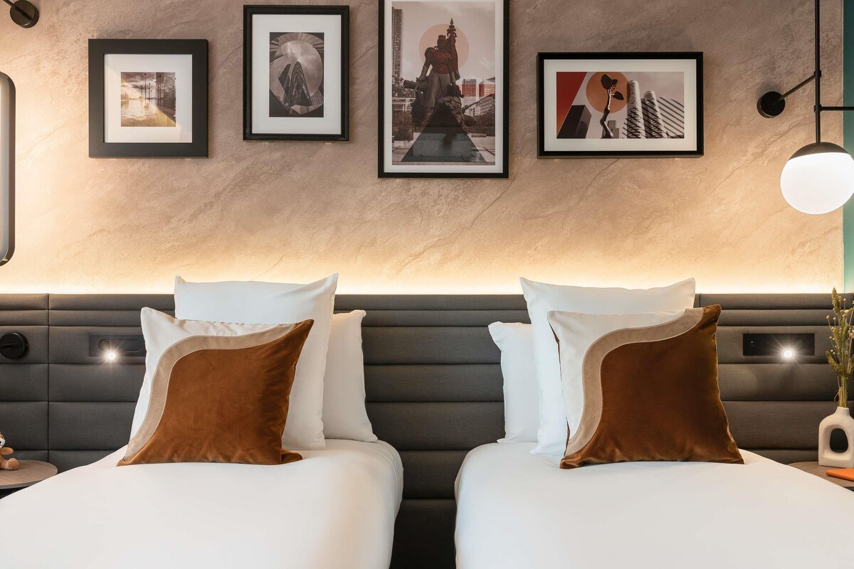 Ein Hotelzimmer mit zwei Betten, einer Marmorwand und gerahmten Kunstwerken.