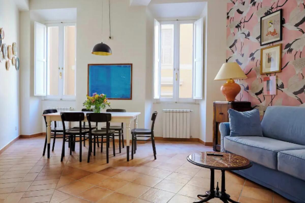 A dining area with a table and chairs, a blue painting on the wall, and a lamp on a side table.