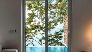 Un soggiorno moderno con un'ampia porta-finestra che dà su un'area piscina, un tavolino in legno e un divano.
