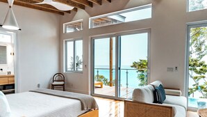 Una camera da letto moderna con pavimento in legno, un letto, una divano e un balcone vista mare.