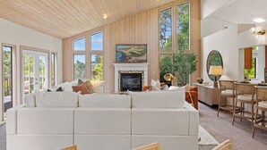 En rummelig stue med en stor, hvid sofa, en pejs og et spiseområde med træstole.