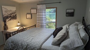 Een slaapkamer met een bed, bureau en stoel. Er is een raam met gordijnen, een schilderij aan de muur en een ingelijste quote.