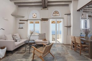 Un salón amplio con sofá, una mesa redonda y una silla de mimbre. Dos puertas dan acceso a un balcón con vistas.