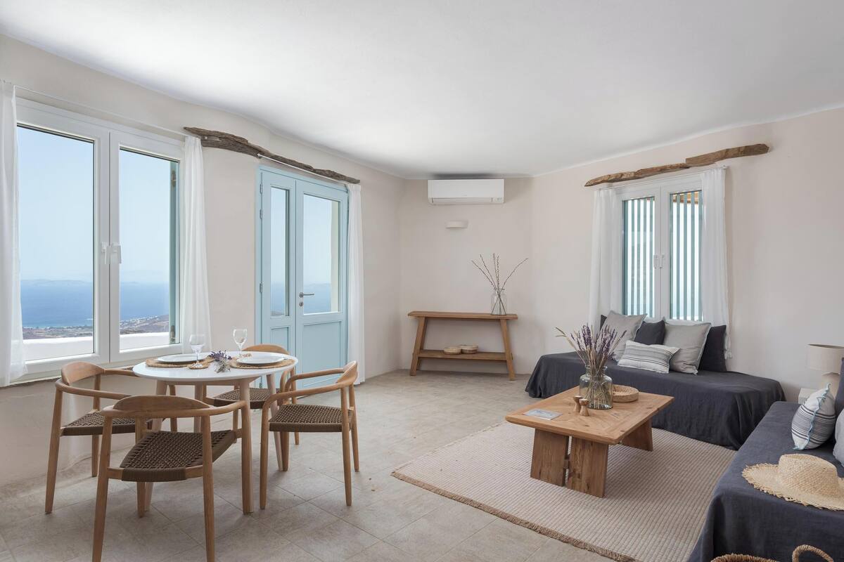 Quarto com área de jantar, sofá, cama e vista para o mar.