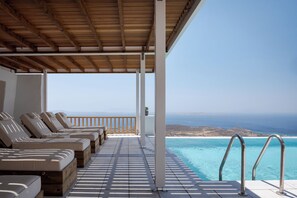 A covered outdoor seating area with lounge chairs and a pool overlooking the ocean. - Morfes Luxury Apartments (Tinos)