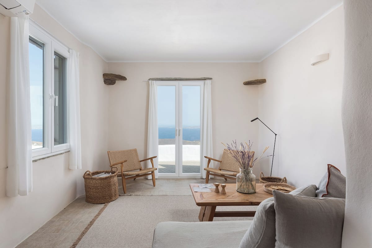 Quarto com vista para o mar, com um sofá, duas cadeiras de vime, uma mesa com um vaso e um abajur.