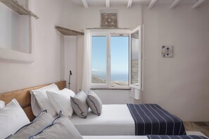 A bedroom with a bed, a window with a view, and a wall-mounted light switch. - Morfes Luxury Apartments (Tinos)