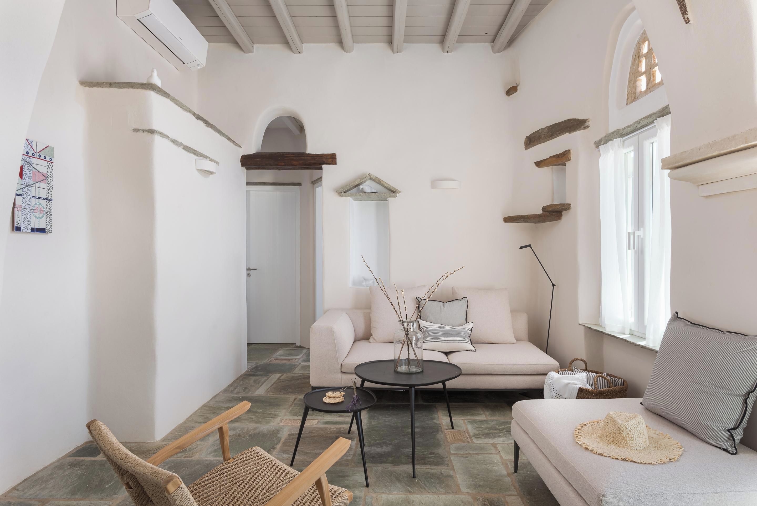 Ein gemütliches Wohnzimmer mit einer Couch, einem Couchtisch und einem Sessel. Ein Fenster mit Vorhängen und einem an der Wand befestigten Regal.