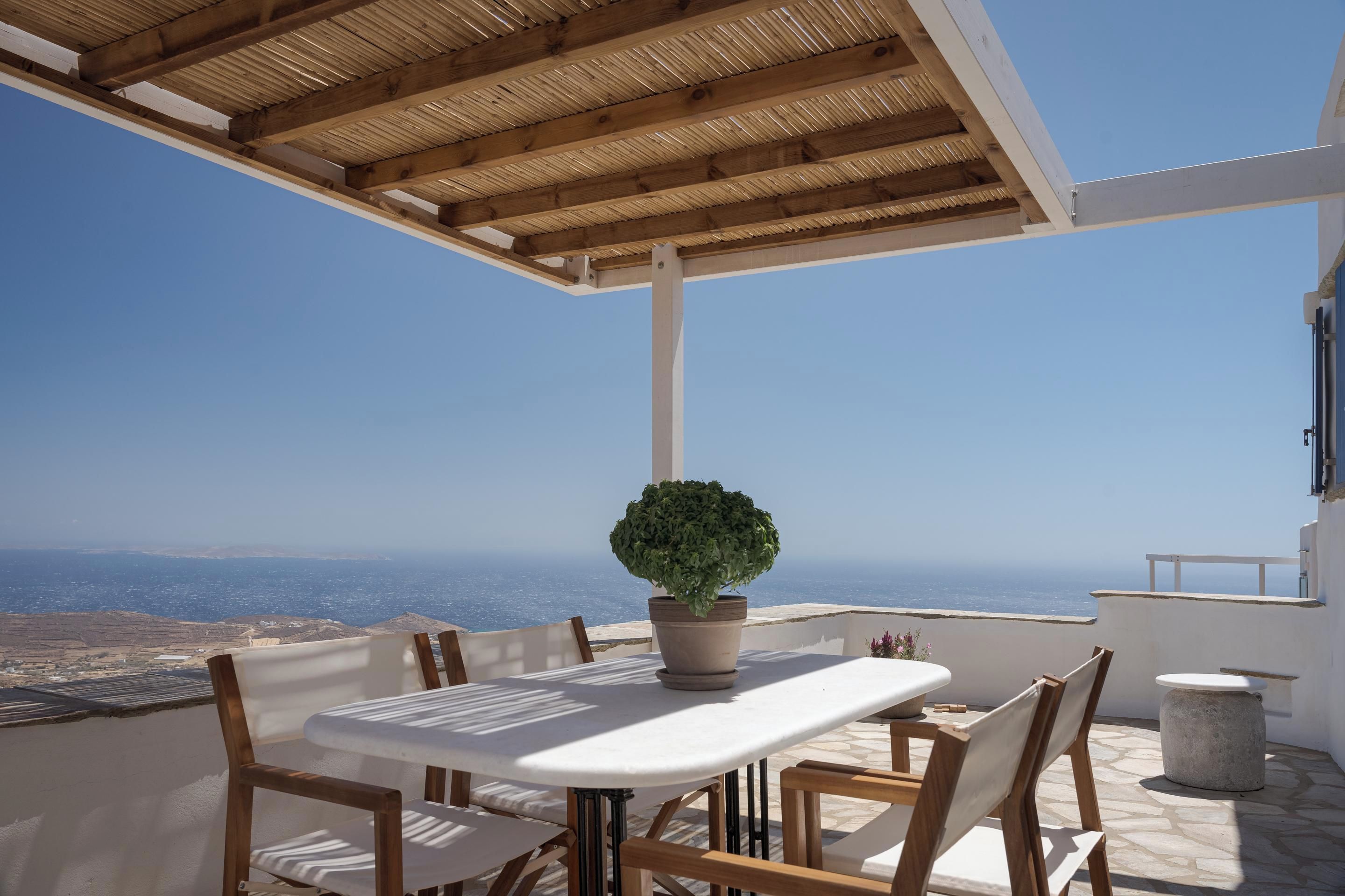 An outdoor patio with a table and chairs, a potted plant, and a view of the sea.