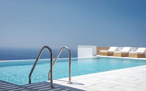 A pool with metal railings and lounge chairs with wooden bases, overlooking a clear blue sky and ocean. - Morfes Luxury Apartments (Tinos)