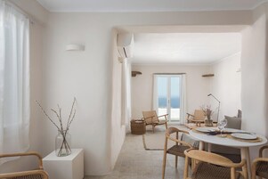 Ένας χώρος τραπεζαρίας με ένα στρογγυλό τραπέζι, καρέκλες από μπαμπού και θέα στη θάλασσα μέσα από ένα μεγάλο παράθυρο.