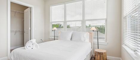 Un dormitorio con una cama grande, una mesita de noche de madera, un taburete redondo de madera y un vestidor.