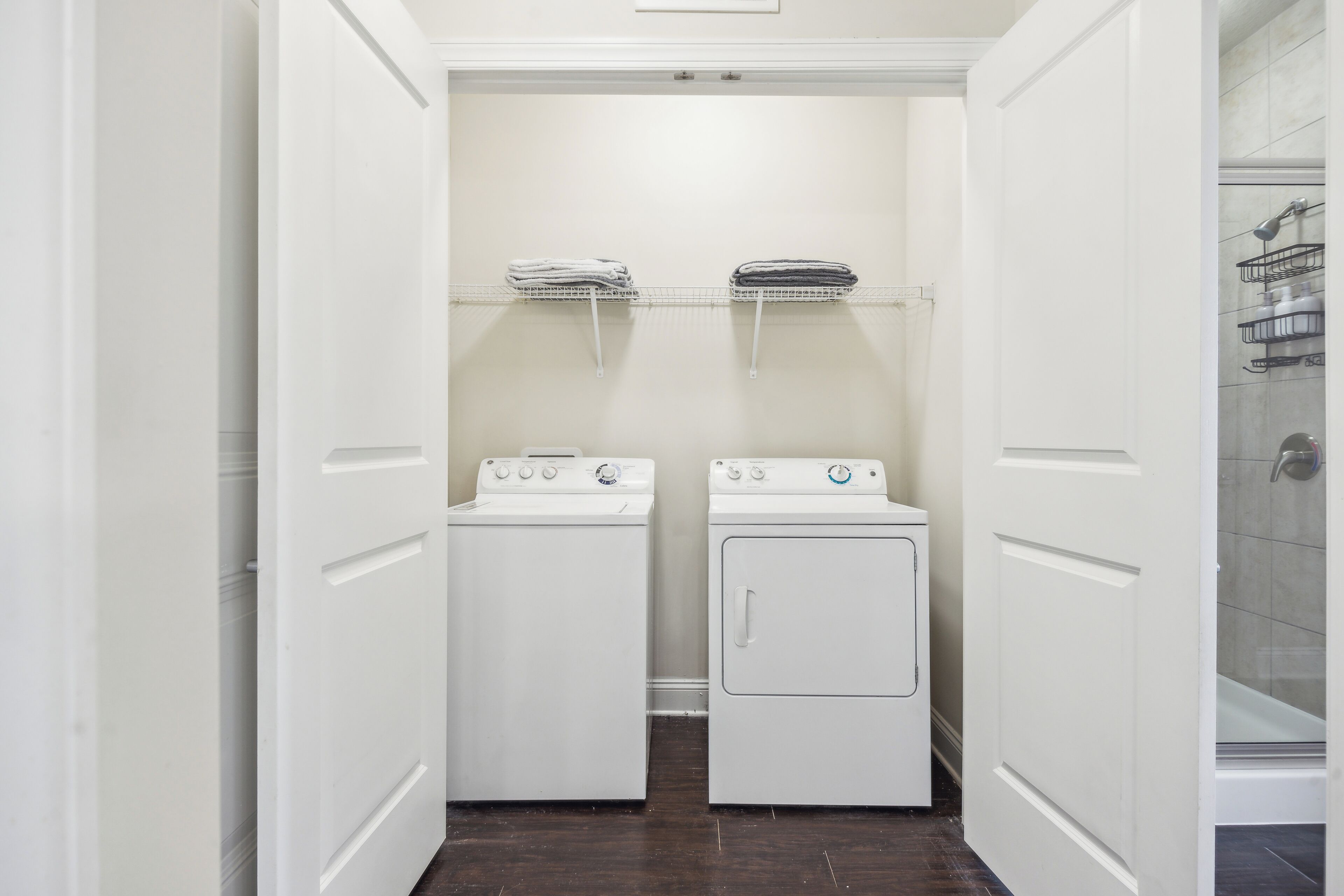 Une buanderie équipée de deux machines à laver et d’un sèche-linge, un espace douche avec une porte en verre et un mur recouvert de carreaux blancs.
