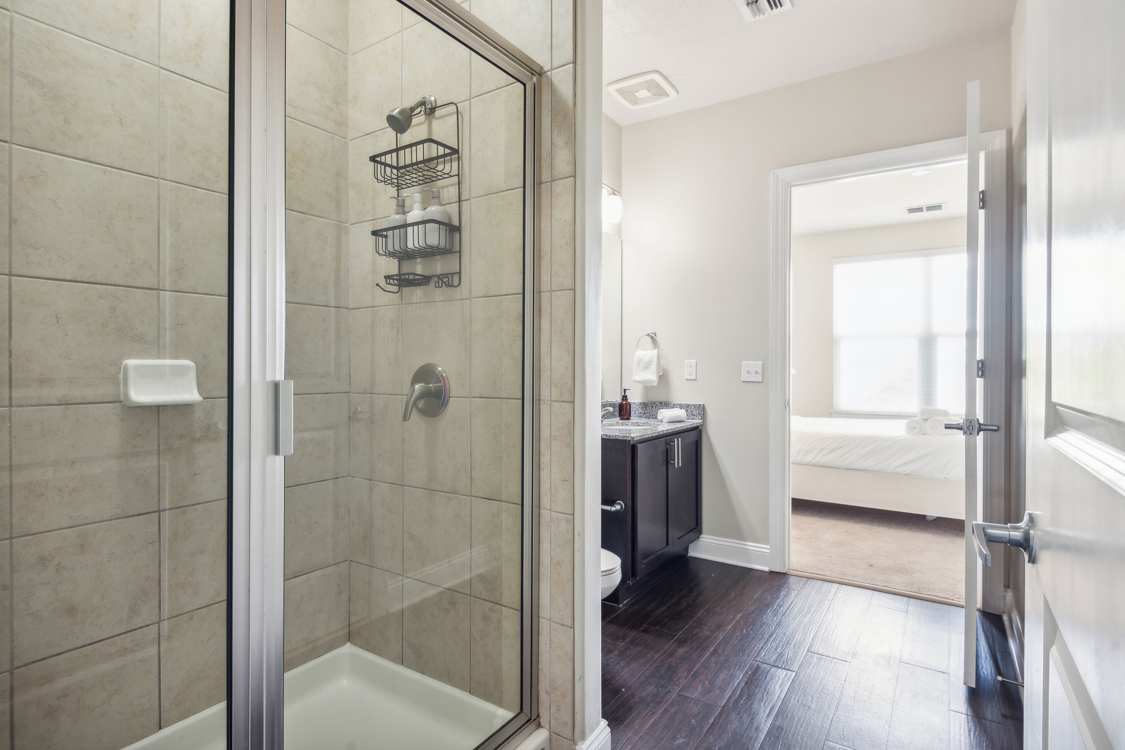 A modern bathroom with a glass-enclosed shower, a dark wood floor, and a white toilet.