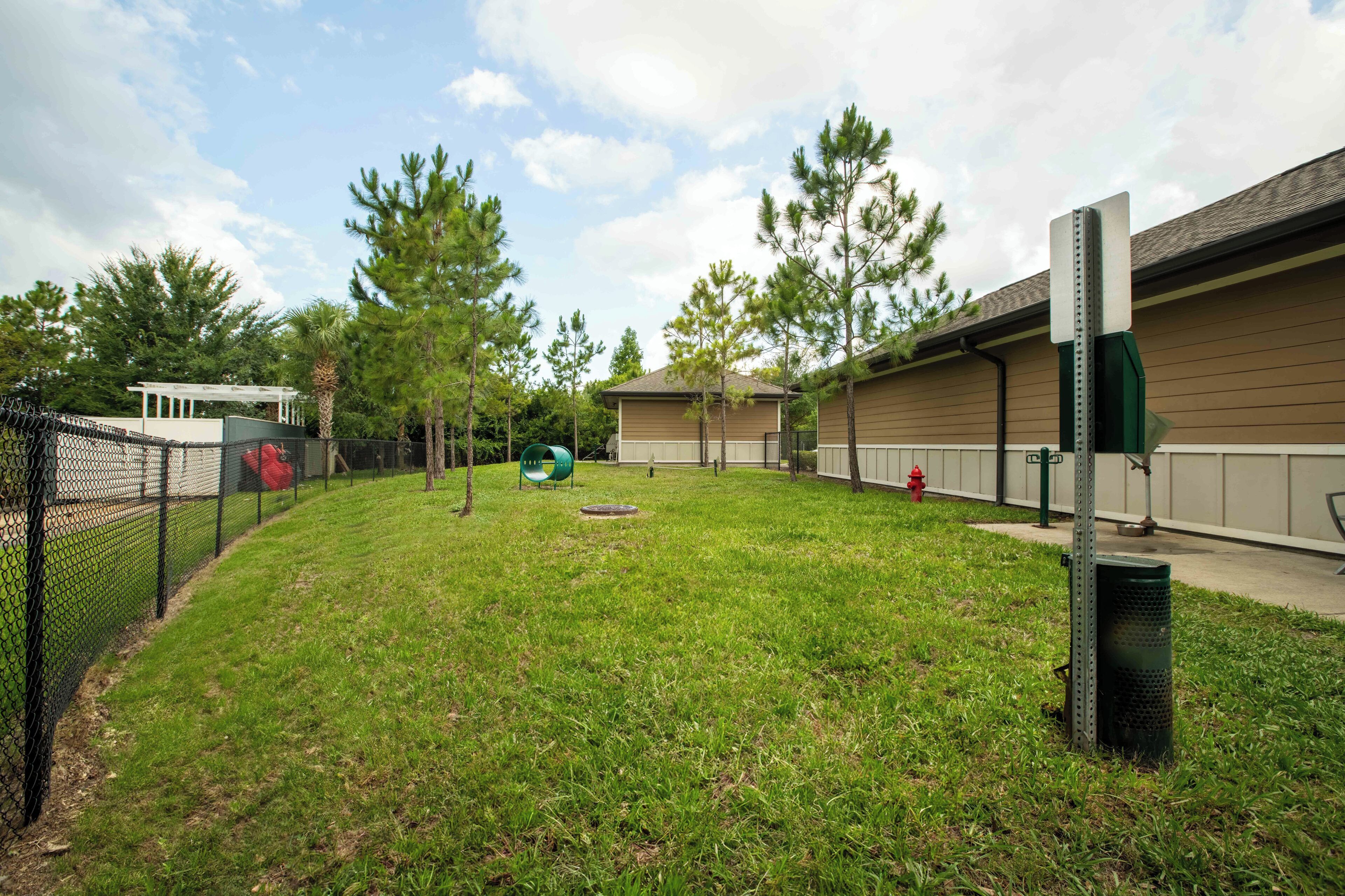 A grassy backyard with a fenced area, a small building, and trees.