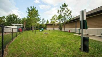 A grassy backyard with a fenced area, a small building, and trees.