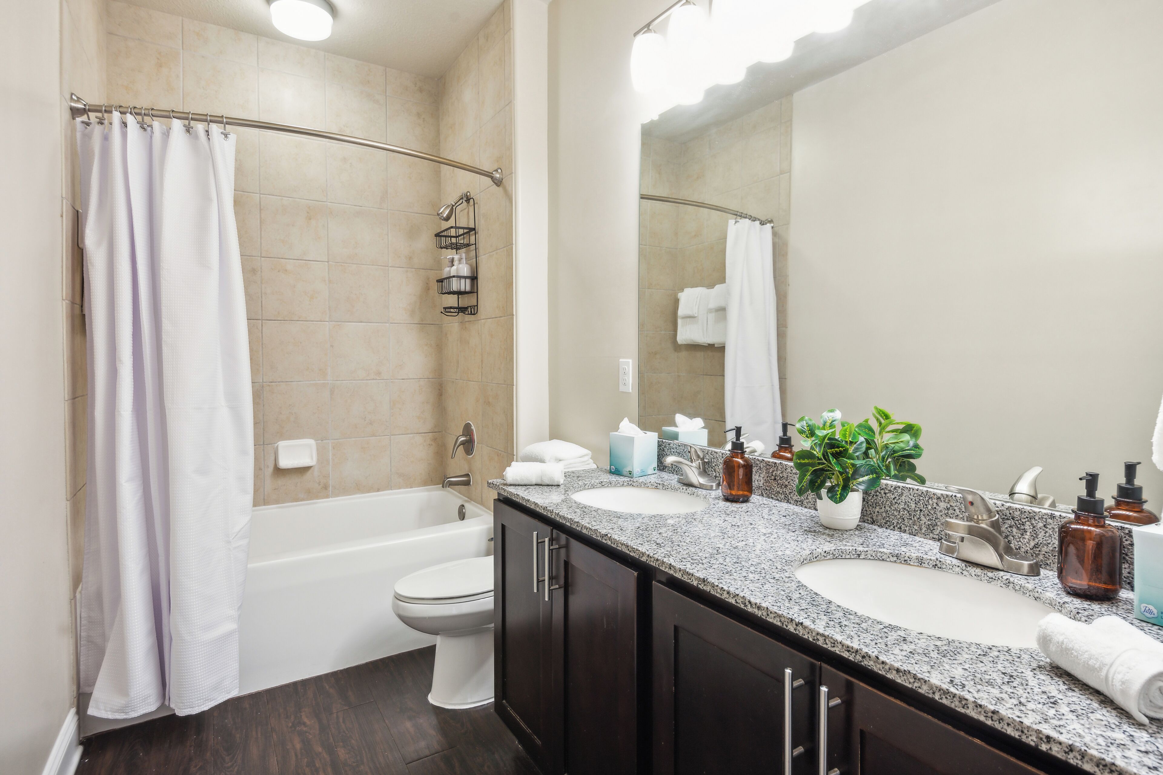 A modern bathroom with a bathtub, toilet, and double sink vanity.