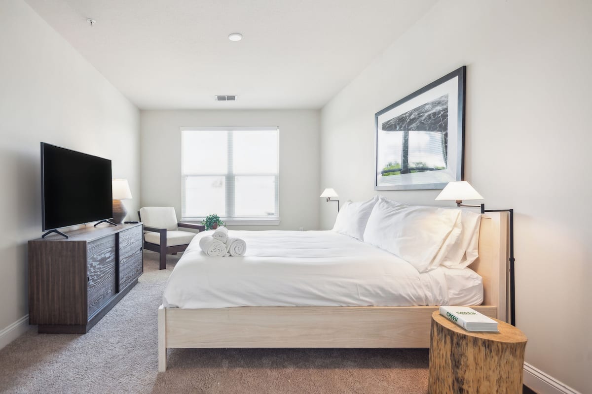 Quarto de hotel com cama, televisão, escrivaninha e janela.