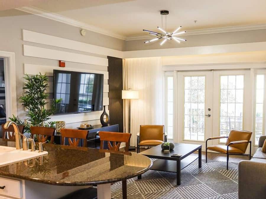 Una habitación de hotel moderna con una zona de cocina, una mesa de comedor y un espacio de estar con sofá y sillones.