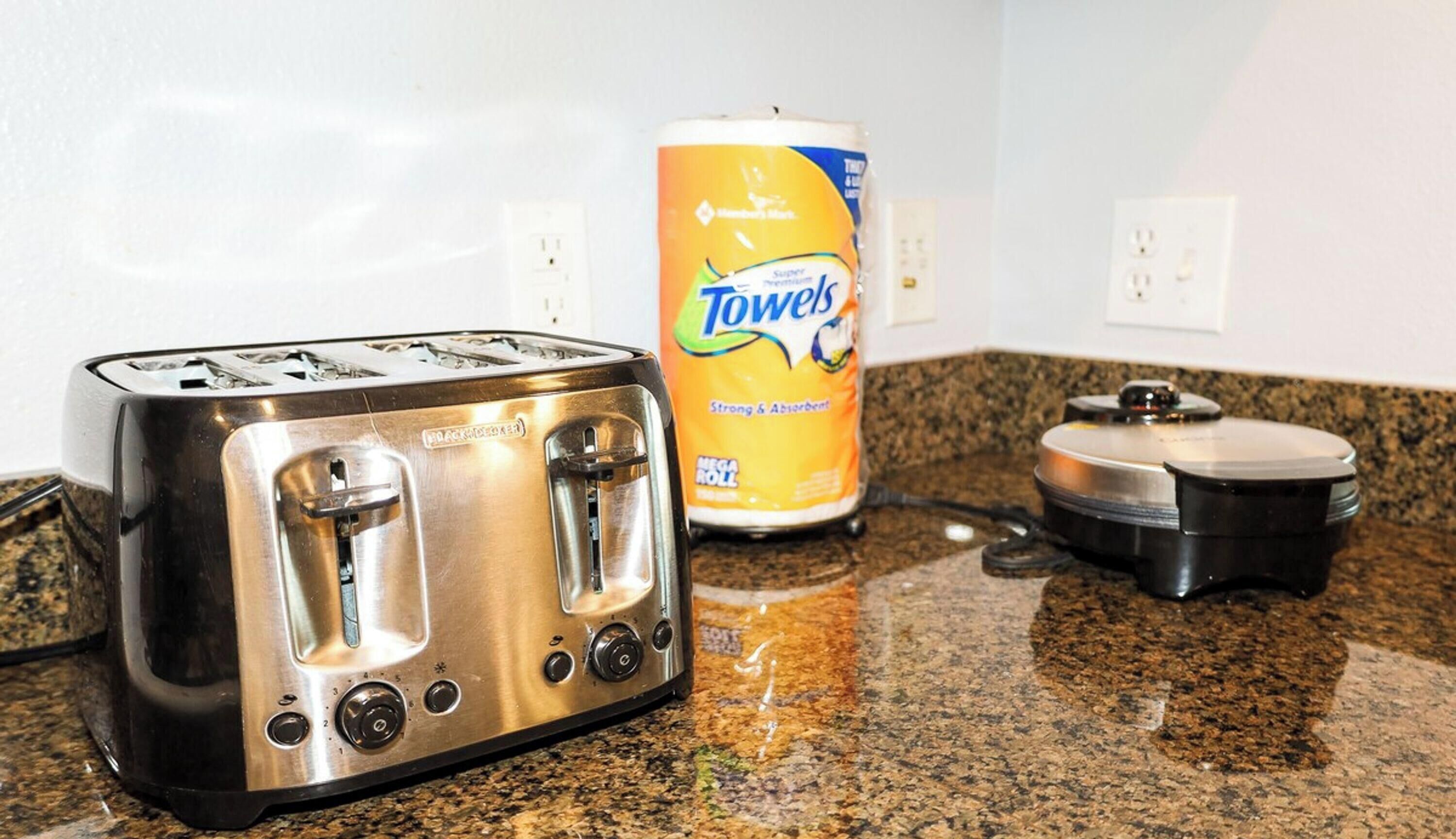 A kitchen counter with a stainless steel toaster, a can of Towels, and a black appliance, possibly a rice cooker.